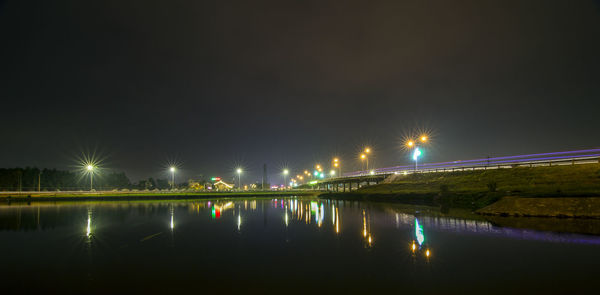 Illuminated street lights by river against sky at night