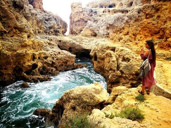 Rear view of woman standing on cliff against sky