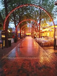 Illuminated footpath amidst trees in city at dusk