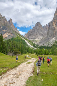 Rear view of hikers walking on meadow against mountain ranges and sky