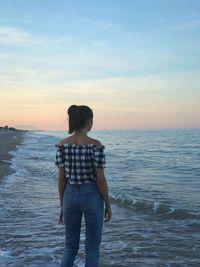 Rear view of woman standing on sea against sky during sunset