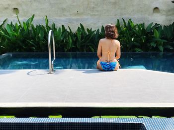 Rear view of shirtless man sitting in swimming pool
