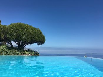 Swimming pool by sea against clear blue sky