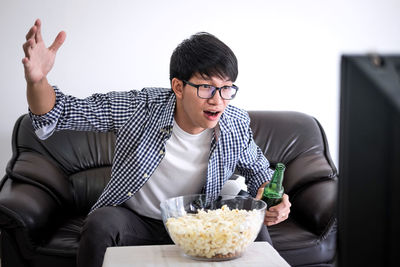 Excited young man watching sport while lying on sofa at home