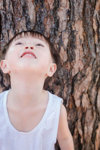 Close-up of boy looking up against tree trunk