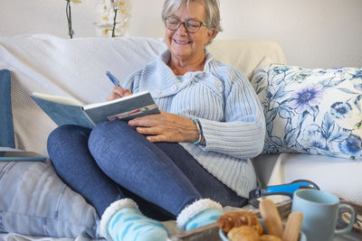 Smiling senior woman writing in diary sitting at home