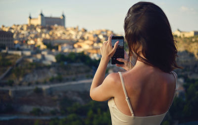 Side view of young woman photographing through mobile phone