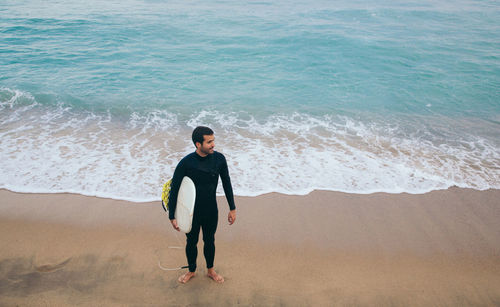 High angle view of young man with surfboard standing at beach