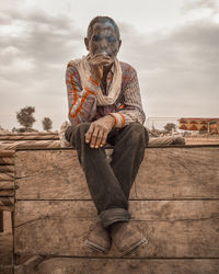 Smoking man sitting on wood against sky