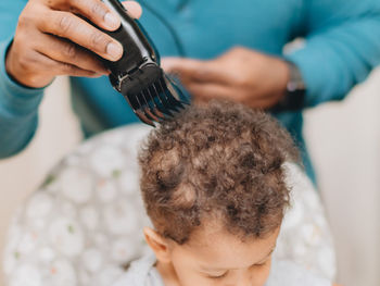 Midsection of mother trimming hair of son at home