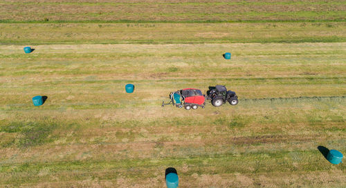 Black tractor with a red straw chamber press during the straw harvest on a mown field