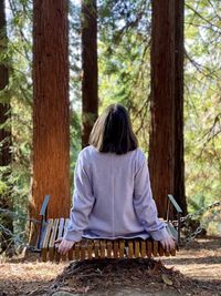 Rear view of woman sitting on swing in forest