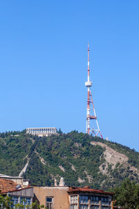 Communications tower amidst buildings against clear blue sky