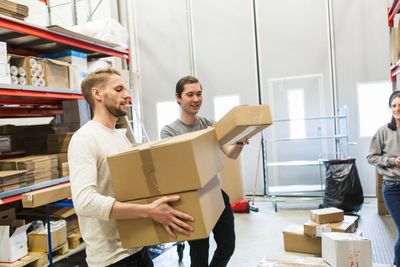 Woman looking at coworkers carrying boxes in distribution warehouse