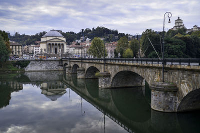 Arch bridge over river by buildings against sky in city