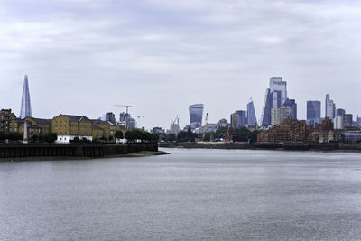 View of buildings by river against cloudy sky