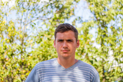 Serious young brunette caucasian man with short hair. summer blurred nature bokeh background. 