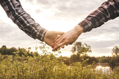 Low angle view of couple holding hands on field against sky