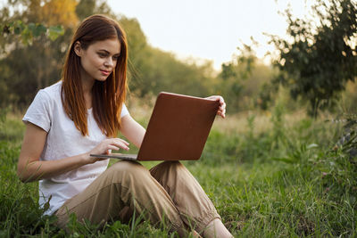 Woman using laptop while sitting on field