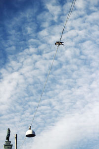 Low angle view of bird perching on cable against cloudy sky