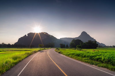 Country road amidst green landscape against sky during sunny day