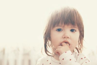 Portrait of cute girl with fingers in her mouth looking at camera