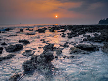 Scenic view of rocks on beach against sky during sunset