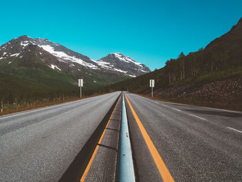 Empty road leading towards mountains against sky