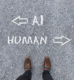 Man looking down at the words artificial intelligence - ai - and human chalked onto the floor