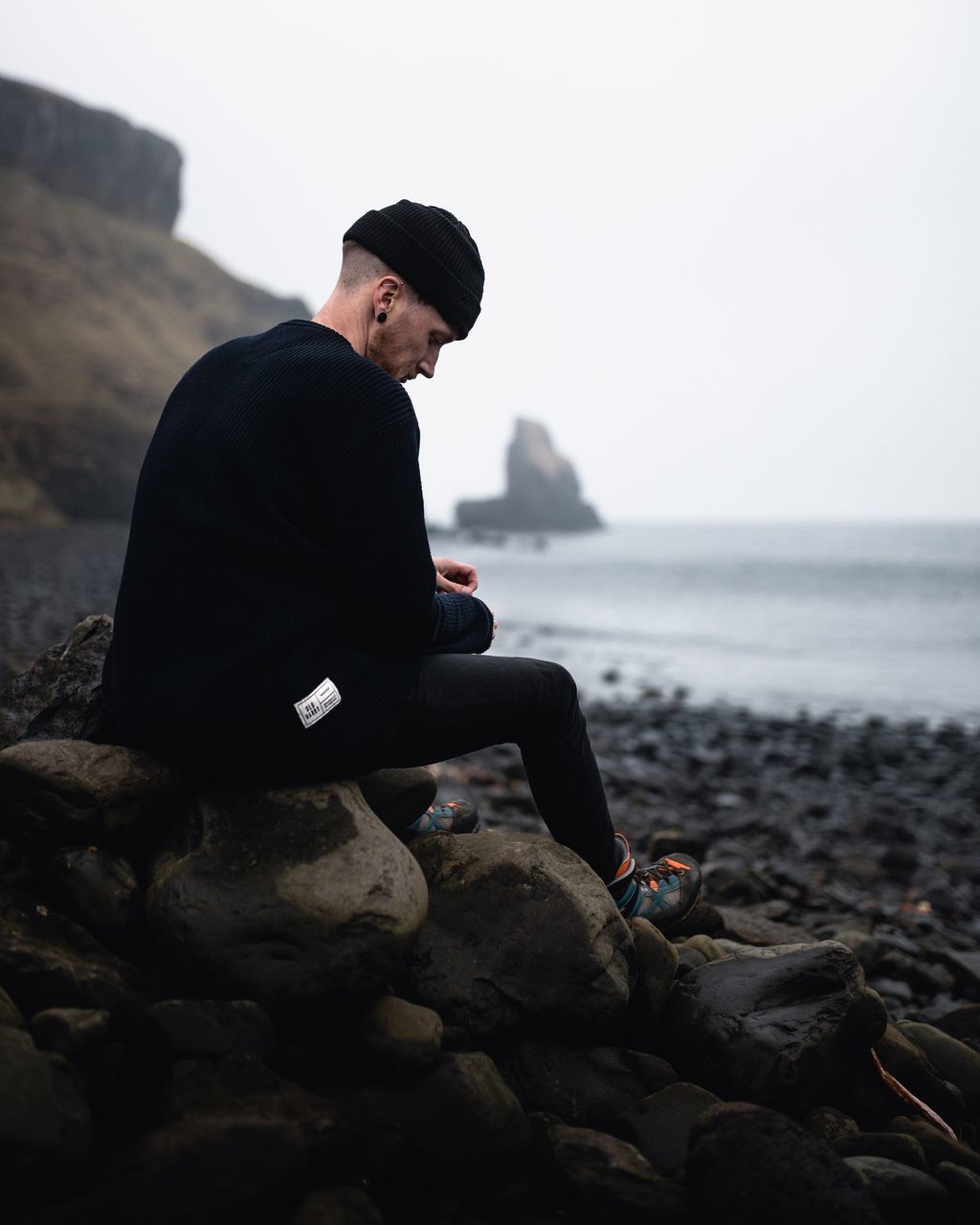 solid, rock, one person, rock - object, real people, sitting, water, sky, land, lifestyles, sea, leisure activity, full length, nature, beach, side view, young adult, young men, horizon over water, outdoors