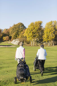 Rear view of senior women walking with golf bags on course