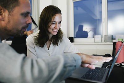 Smiling female business professional working over laptop with male colleague at office