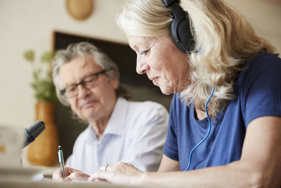 Senior vlogger with headphones writing while sitting with man at home