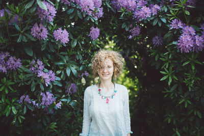Portrait of smiling woman standing by purple flowering plants