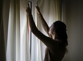 Young woman opening the curtains of the room in the morning.