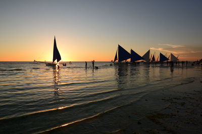 Silhouette sailboats in sea against sky during sunset