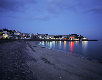 Illuminated buildings by sea against sky at dusk