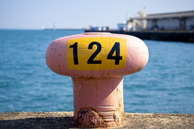 Close-up of information sign on pole against sea