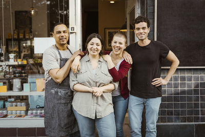 Portrait of happy multiracial male and female business owners standing outside store