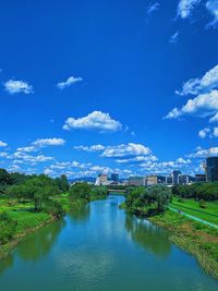 Scenic view of river by buildings against blue sky