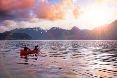 Man on boat in lake against sky during sunset