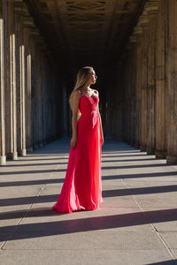 Full length of young woman in pink evening gown standing at colonnade
