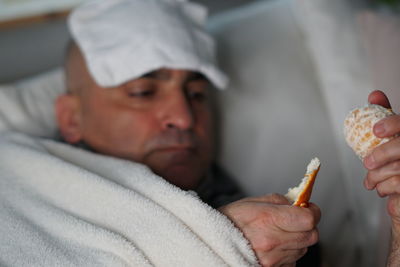 Close-up of man having orange while lying on sofa