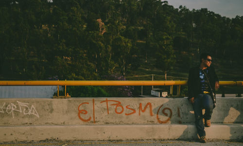 Woman standing by retaining wall against trees