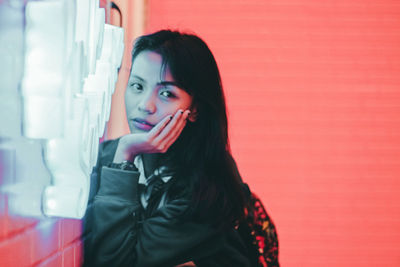 Portrait of beautiful young woman standing against red wall