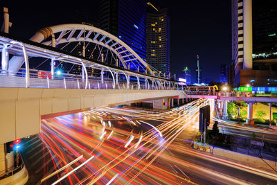 Light trails on road by illuminated buildings at night