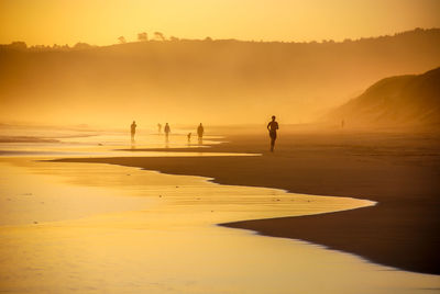 Silhouette people at beach during sunset in foggy weather