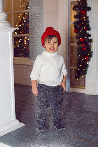 Boy stands on the porch of the house in a sweater and a red hat