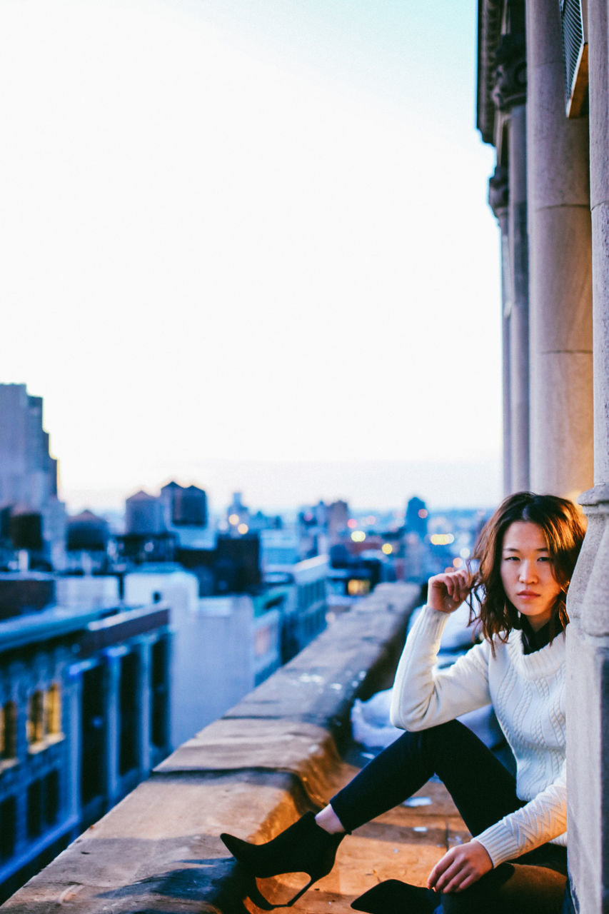 lifestyles, building exterior, architecture, built structure, city, focus on foreground, leisure activity, water, clear sky, railing, river, casual clothing, cityscape, young adult, person, headshot, rear view, waist up