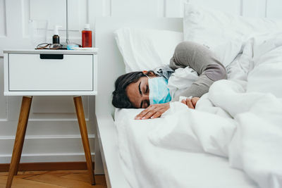 Ill woman wearing mask relaxing on bed at hospital